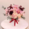 Mixed pinks and burgundy arrangement in a white ceramic vase.
Flowers may include