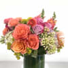 Lush arrangement bursting with orange and lavender florals set in a ti