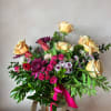 Bursting with color, this arrangement features brilliant orange roses, alongside purple and