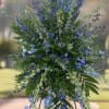 Blue delphinium And Thistle with mixed greenery on an easel.