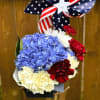 Blue hydrangea, white and red carnations are topped with an American Flag