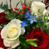 A vibrant mix of red roses, white blooms, and soft blue accents.