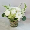 A clear glass cylinder with a green hydrangea, white ranunculus, white cremons