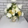 A white and gold glass container arranged with artificial white ranunculus, white