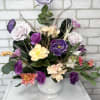 A white urn arranged with artificial lavender, purple, and peach florals and