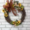 A grapevine wreath arranged with artificial mini sunflowers, daisies, mixed greens, and