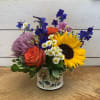 Sunflowers, orange roses, bright blue belladonna, and a large lavender crysanthemum arranged
