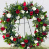 A large wreath filled with White Cushion Mums, Red Roses and Blue