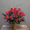One dozen red roses with seasonal greens and filler in a vase.
