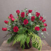 One dozen red roses with seasonal greens and filler in a vase.