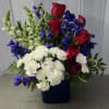 This is a patriotic-style floral arrangement in a bold navy blue square