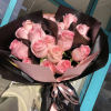 A front-facing bouquet of roses with layered paper accents, wrapped in black
