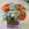 A 4X4 square vase with blue hydrangea and orange roses.  Vase