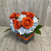 A 4X4 square vase with blue hydrangea and orange roses.  Vase