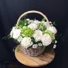 A lovely basket full of white roses and green hydrangeas nested in