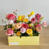 A yellow rectangular box filled with coral, pink, white, and yellow flowers.