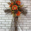 A hanging grapevine cross arranged with a mix of artificial fall florals.