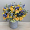 Blue delphinium, yellow spray rose, yellow tulips and seasonal greenery come together