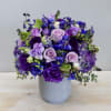 This arrangement showcases delphiniums in dark blues, lavender roses, and purple lisianthus