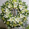 Elegant sympathy wreath featuring stunning white lilies, soft ivory roses, and lush