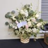A wispy white and green basket featuring silver dollar eucalyptus and white