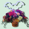 A jack-o-lantern tin is overflowing with autumn colored mums, carnations, mini carnations
