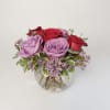 A clear glass bubble bowl filled with 6 roses and lavender waxflower.