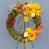 This artfully designed tribute features sunflowers, roses, seasonal textures and fresh moss.