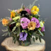 A vibrant medley of lavender roses, golden blooms, and fresh greenery arranged