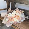 A softly wrapped bouquet in shades of ivory, blush, and peach, designed