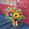 This seasonal arrangement of burgundy lilies, red roses, butterscotch mums, bright sunflowers
