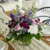 Seasonal blooms of lavender roses, burgundy mums, blue delphinium, and white chrysanthemums