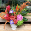 Assorted tropical blooms mixed with seasonal flowers in a pedestal vase.
