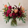 A lush mix of vibrant roses, deep burgundy lilies, and peach accents
