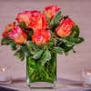 A dozen beautiful roses set in a cube vase with lush greens.