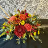 A beautiful arrangement of fall toned flowers in a low centerpiece container.