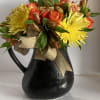 A pitcher filled with bright orange and yellow seasonal blooms.