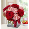  6 red roses arranged with pink mini carnations in a clear