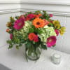 Orange, pink and green flowers arranged in a clear glass vase. Featuring