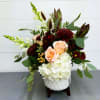 A beautiful modern white keepsake container is filled with white hydrangeas, peach