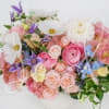 Soft and romantic, this pastel arrangement features roses, ranunculus, lisianthus, delphiniums, and