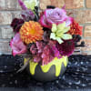 A whimsical Halloween arrangement designed in a black cauldron-style baking container, brimming