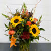 This tall, clear vase is filled with sunflowers, orange lilies, orange roses