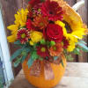 A freshly cut orange pumpkin filled with traditional fall flowers