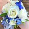 This wrist corsage features white spray roses and blue delphinium