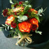 Fall colored Roses and Carnations with seasonal greenery in a clear vase