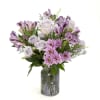 A lavender tinted vase filled with shades of lavender and purple flowers