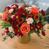 A cheerful mix of orange roses, mums, and soft blush blooms in