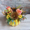 A ceramic yellow/orange pumpkin filled with fall blooms. Roses, mums, berries, and