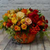 The pumpkin arrangement includes roses of different shades, orange berries and greenery.